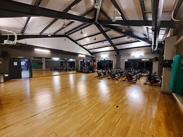 Sala polivalente, con suelo de parqué, espejo y puerta de acceso y bicicletas de "spinning" al fondo