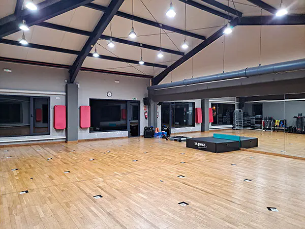 Vista en detalle de una zona de la sala polivalente, con un gran espejo y diversos accesorios deportivos