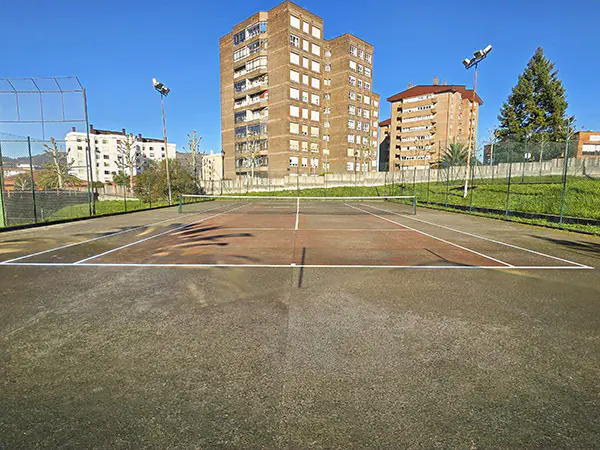 Panorámica de una de las pistas exteriores de tenis, con vista al fondo de edificios