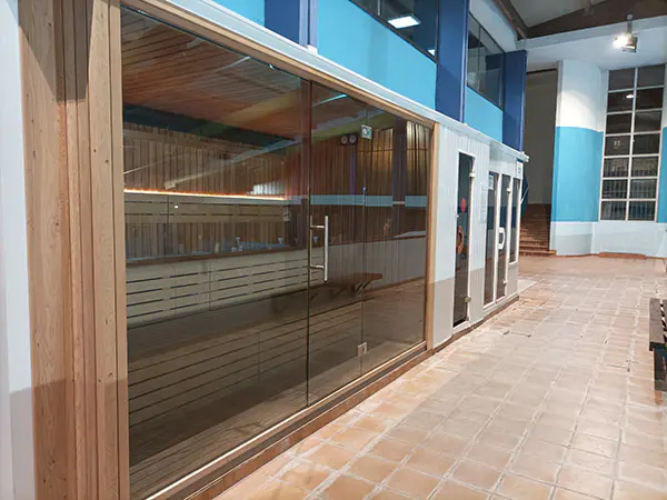 Sala de sauna, con vista lateral de los bancos de madera de su interior a través de la cristalera exterior