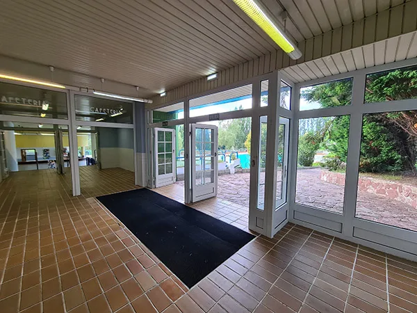 Vestíbulo de distribución, con puerta de acceso a la cafetería y puerta exterior de salida a las piscinas