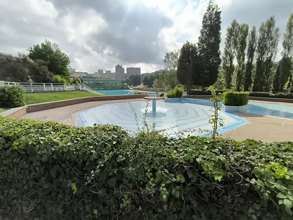 Piscina infantil con una fuente central interior y rodeada de jardines y árboles  