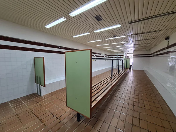 Vestuario con bancos de madera con perchas en el centro y bancos de azulejo adosados a las paredes