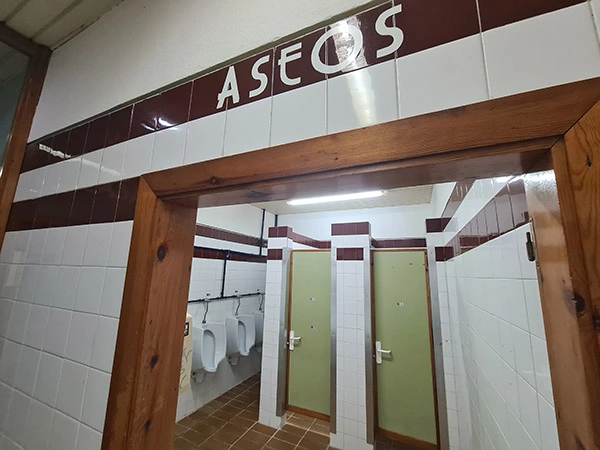 Puerta de acceso a los aseos, con urinarios en un lateral y cabinas de retretes en el centro