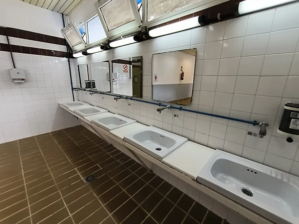 Aseos con una fila de lavabos con espejos, secador y jabonera de pared