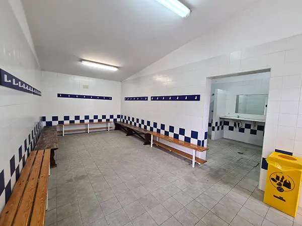 Vestuario: azulejos blancos, percheros blancos sobre banda azul. Dos hileras azulejos azules alternos sobre bancos de madera 
