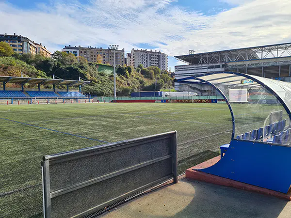 Vista parcial del terreno, con uno de los banquillo en primer plano y al fondo, una portería y las gradas cubiertas
