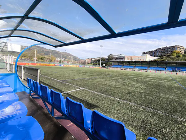 Vista del campo desde el interior del banquillo, con detalle de las sillas y la cubierta transparente 