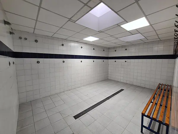 Interior de las duchas de los vestuarios, con paredes de azulejo, un banco de madera y percheros