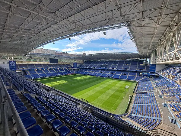 Detalle angular del techo metálico de las tribunas del Estadio, las cuatro tribunas y un rectángulo de cielo celeste y nubes 