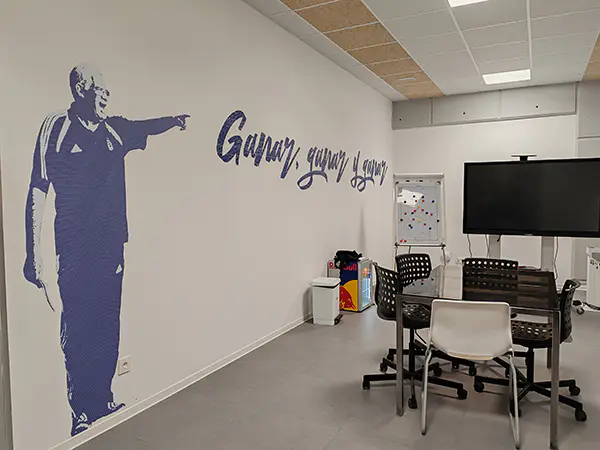 Sala técnica. Muro lateral decorado con imagen de Luis Aragonés de pie señalando y frase en azul: "Ganar, ganar y ganar"