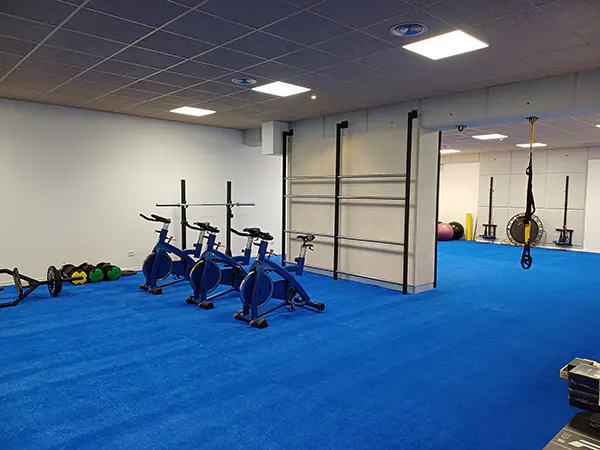 Área del gimnasio con tres bicicletas fijas, soga, tres softball para pitales, alfombra de impacto en azul