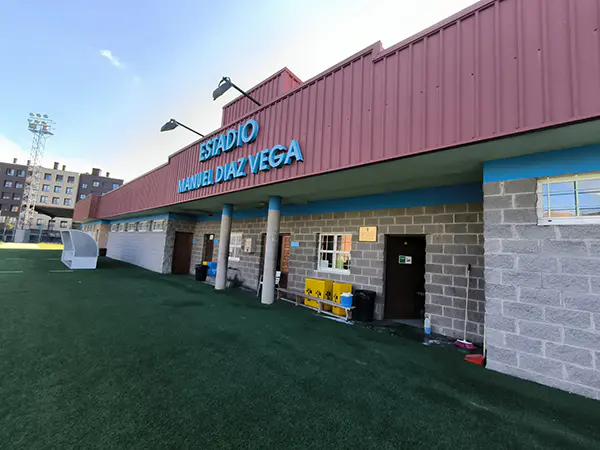 Fachada del edificio principal de las instalaciones, con las puertas de acceso y un cartel con el nombre del estadio