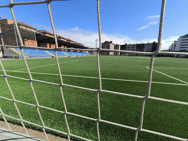Vista del campo desde detrás de una de las porterías, con las gradas en un lateral y edificios al fondo