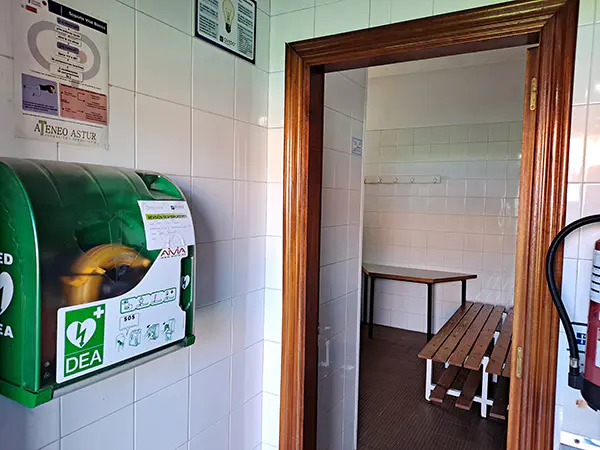 Desfibrilador de pared, junto a la puerta de acceso al vestuario, con bancos de madera en su interior