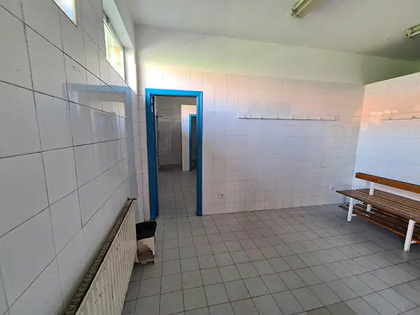 Vista interior de los vestuarios, con paredes de azulejos, un banco de madera y un radiador