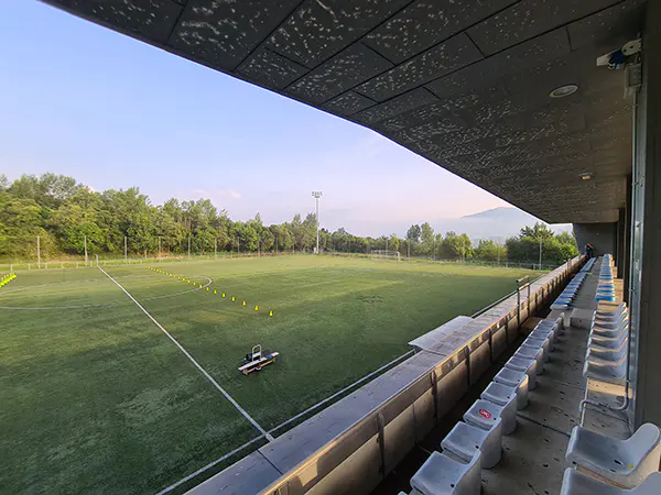 Panorámica de un campo de fútbol 11 desde las gradas, con conos de entrenamiento sobre el césped