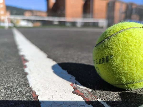 Vista a ras de suelo de una pelota de tenis sobre una de las pistas, con detalle de una línea lateral
