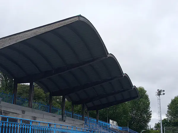 Gradas de cemento con cubierta ondulada, con barandillas de separación y una torre de iluminación al fondo