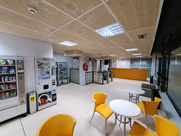 Área de recepción del Centro Deportivo de Otero, con máquinas expendedoras, mesas, sillas y mostrador al fondo