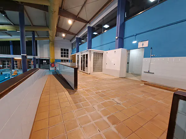 Panorámica de la puerta y pasillo de acceso a la piscina, con las cabinas de spa al fondo