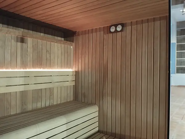 Vista interior de la sauna, con paredes y asientos de madera e indicadores de humedad y temperatura