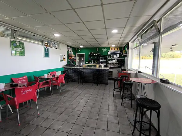 Interior de la cafetería con el mostrador al fondo, mesas y sillas de color rojo en los laterales