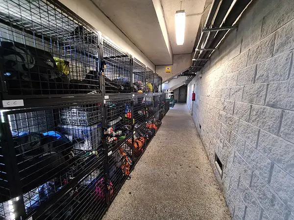 Pasillo con equipamiento deportivo guardado en taquillas negras enrejadas dispuestas en un lateral