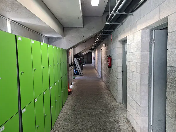 Pasillo con taquillas verdes dispuestas a la izquierda y vestuarios a la derecha