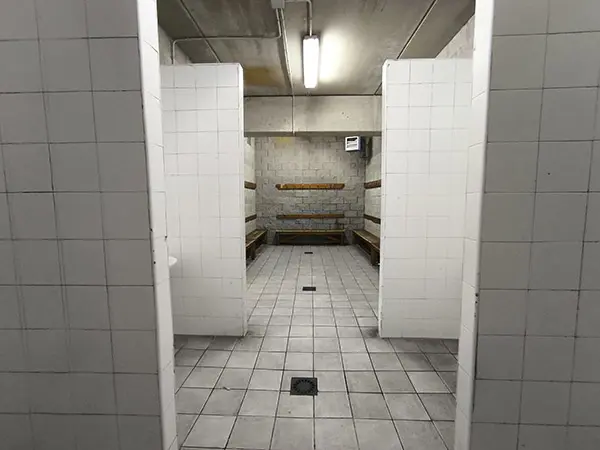 Interior del vestuario con la zona de los lavabos en primer plano y los bancos y percheros de madera al fondo