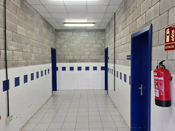 Pasillo interior en color gris con zócalo en color blanco y azul , y puertas azules de acceso a vestuarios