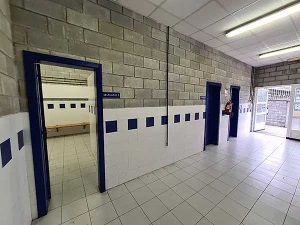 Entrada al vestuario con puerta y rótulo de color azul en un pasillo otras dos estancias y al fondo la puerta de entrada