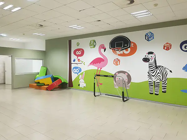 Área de servicios infantiles, con un mural con dibujo de animales, canasta de minibasket y diversos accesorios infantiles