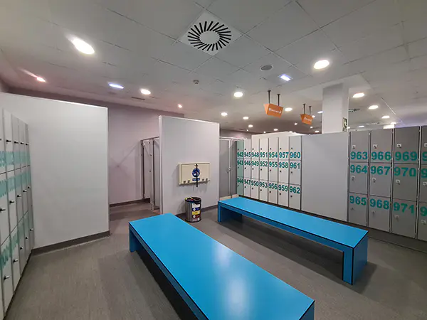 Interior de los vestuarios femeninos, con bancos, taquillas y cambiador de pañales horizontal plegable