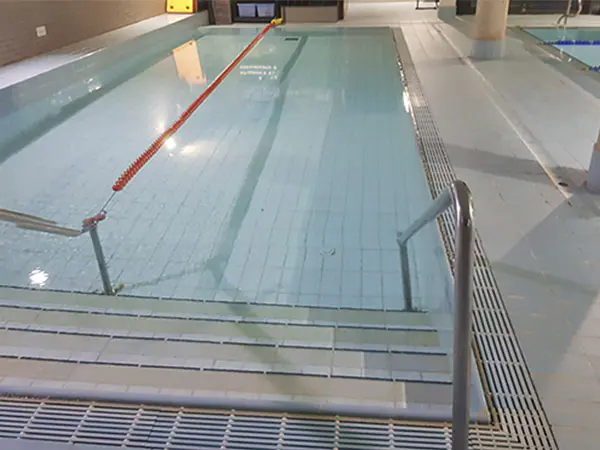Piscina de aprendizaje climatizada, con las escalerillas de acceso en primer plano y una cuerda de seguridad