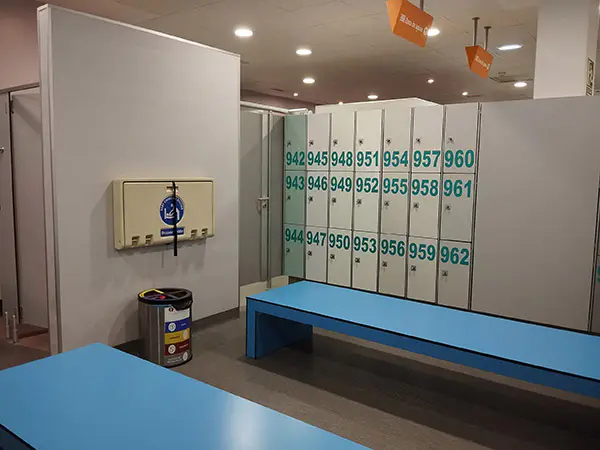 Interior de los vestuarios femeninos, con bancos, taquillas y cambiador de pañales horizontal plegable