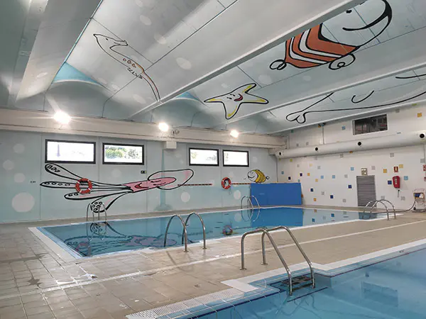 Detalle de las piscinas de aprendizaje, con barandillas de acceso y pinturas de peces, de carácter infantil, en las paredes