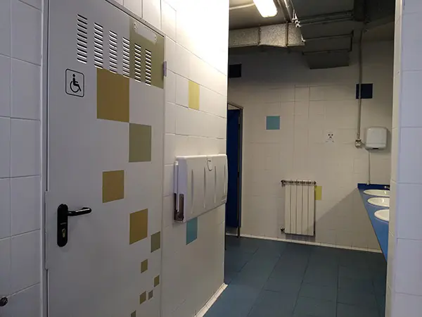 Detalle de los aseos, con vista de la puerta de entrada al aseo para personas con discapacidad
