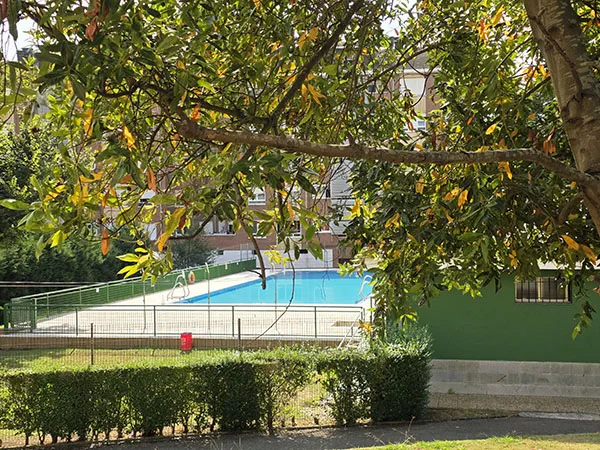 vista de las instalaciones desde el exterior. Edificio de servicios en primer plano y piscina detrás
