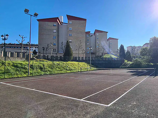 Panorámica a pie de pista y desde una esquina de una cancha de tenis, con las vallas perimetrales y edificios al fondo