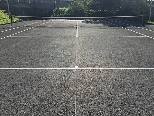 Vista en detalle, a pie de pista, de una de las canchas de tenis, con la red central y las líneas de juego